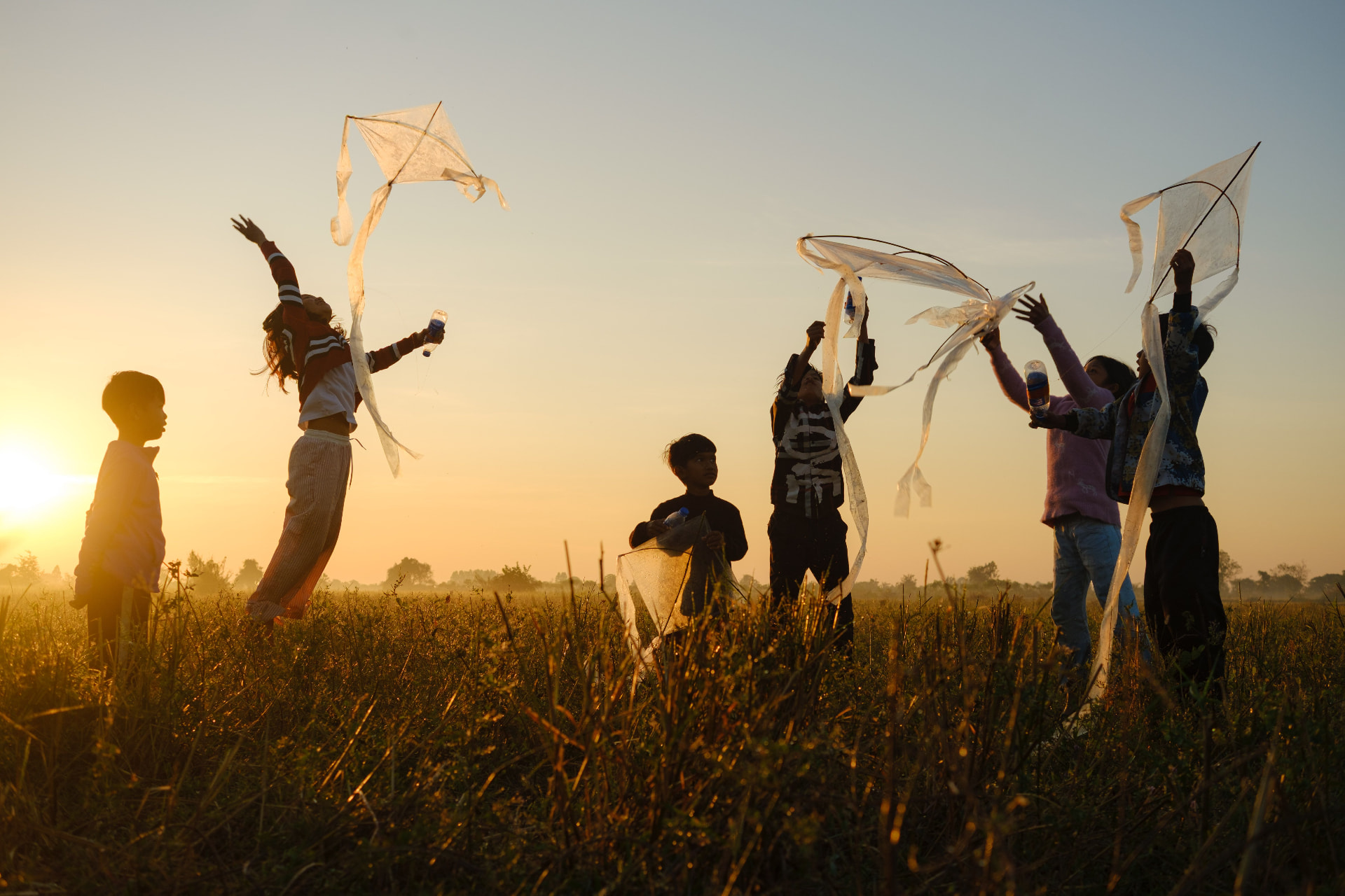 Crianças empinando pipas em um campo ao pôr do sol
