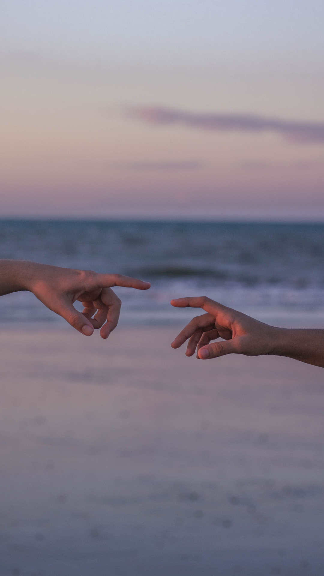 Duas mãos se aproximando diante do mar ao entardecer